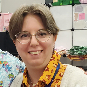 A person in glasses and fun collared shirt smiling.